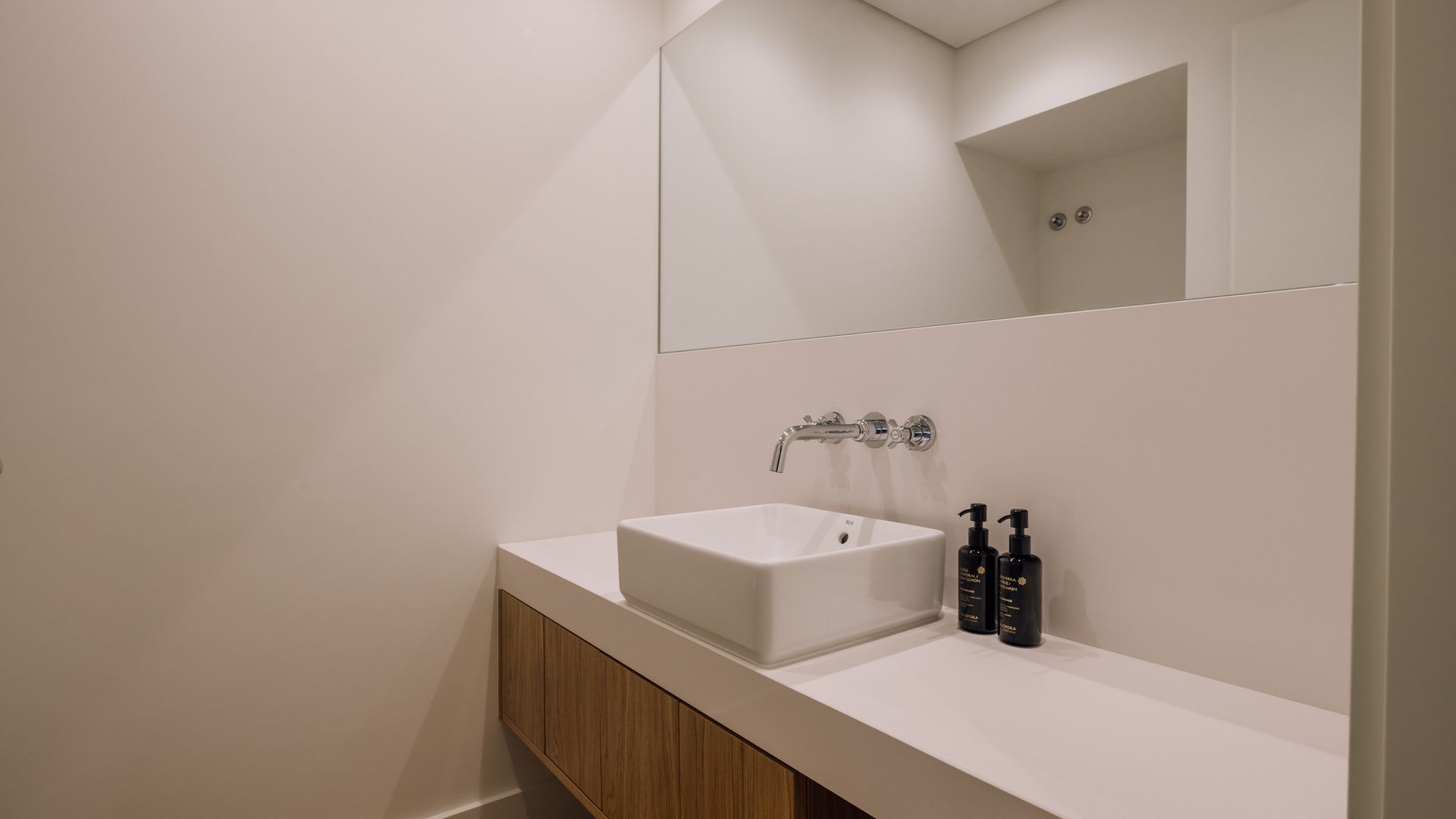 Een moderne badkamer met een wit wastafelmeubel, een houten kast en een grote spiegel.