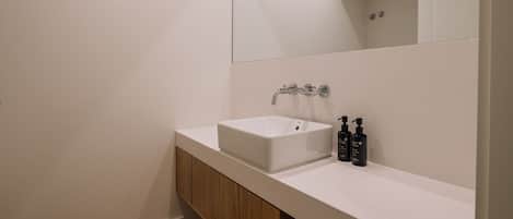 A modern bathroom with a white sink, wooden cabinet, and a large mirror.