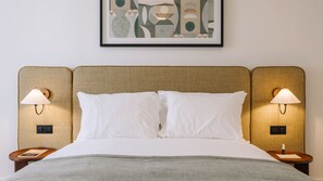 Ein Hotelzimmer mit einem Bett, zwei Nachttischlampen, einem gerahmten abstrakten Kunstwerk und einem kleinen Tisch mit einem Buch.