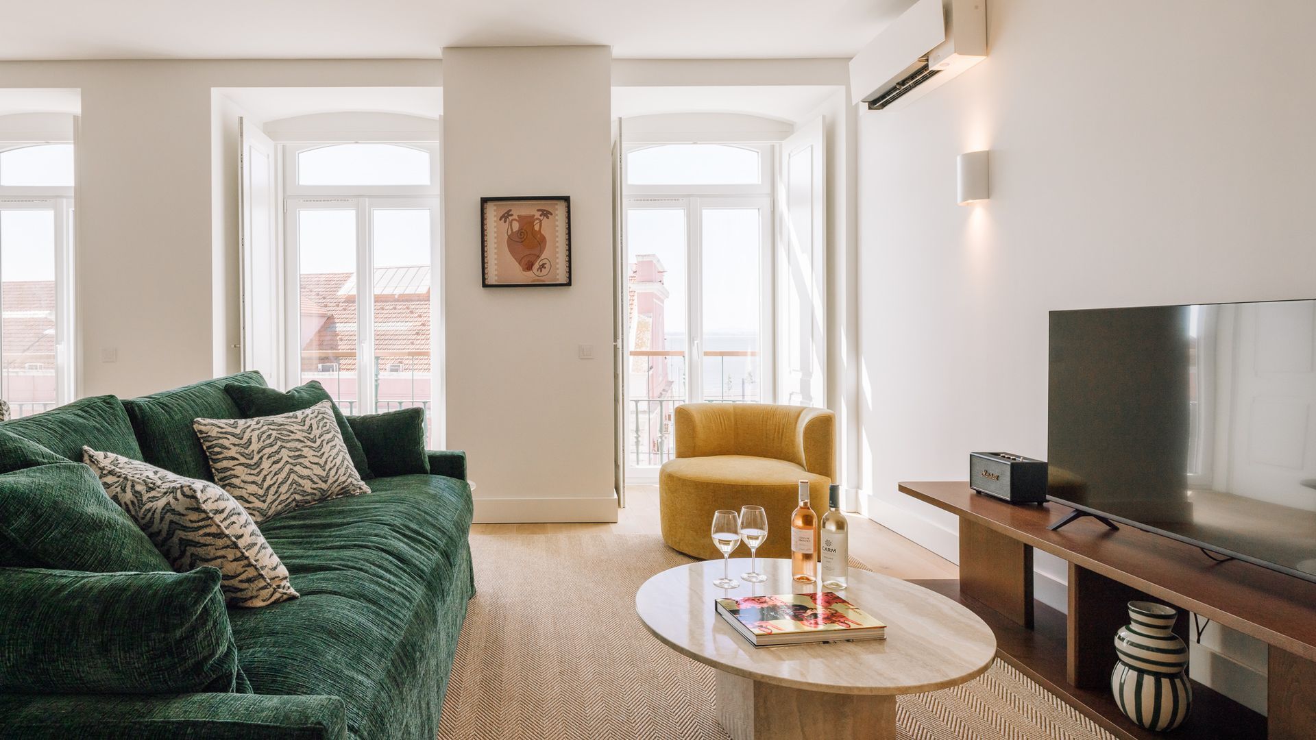 A modern living room with a green sofa, a yellow armchair, a round coffee table with a magazine, and a flat-screen TV on a wooden stand.
