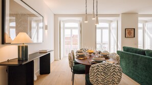 A dining area with a table set for four, chairs with patterned upholstery, a modern lamp, and a green sofa. - Ando Living - Tejo Palace - 201 (Lisboa)