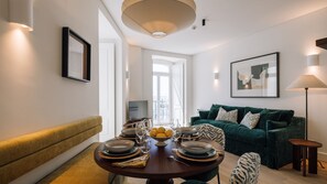 A modern living room with a round dining table set for four, a green sofa, and a large window providing natural light. - Ando Living - Tejo Palace - 202 (Lisboa)