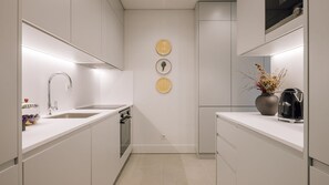 A modern kitchen with white cabinetry, a stainless steel sink, and a built-in oven. There are decorative plates on the wall and a vase with dried flowers on the counter. - Ando Living - Tejo Palace - 202 (Lisboa)