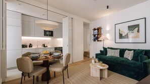 A modern living room with a green sofa, a dining table with chairs, and a kitchen area with white cabinets and a microwave. - Ando Living - Tejo Palace - 203 (Lisboa)