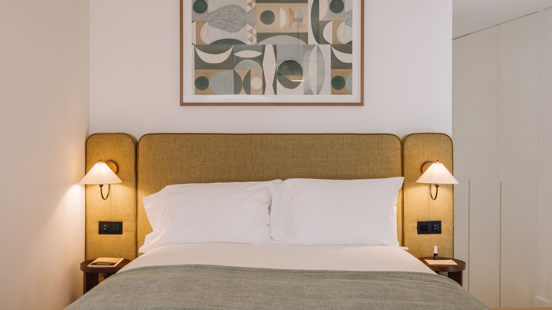 Ein Hotelzimmer mit einem Bett, zwei Nachttischlampen, einem Nachttisch, einem Wandbild und einer Tür.