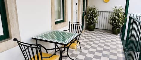 Eine Terrasse im Freien mit Schachbrettmuster, einem Tisch, Stühlen, Blumentöpfen und einem Geländer.
