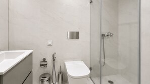 Et moderne badeværelse med et glasvæg-afskærmet brusebad, toilet og håndvask.