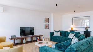 A modern living room with a flat-screen TV, teal sofas, a coffee table, and a framed artwork on the wall. - Ando Living - Tejo Palace - 301 (Lisboa)