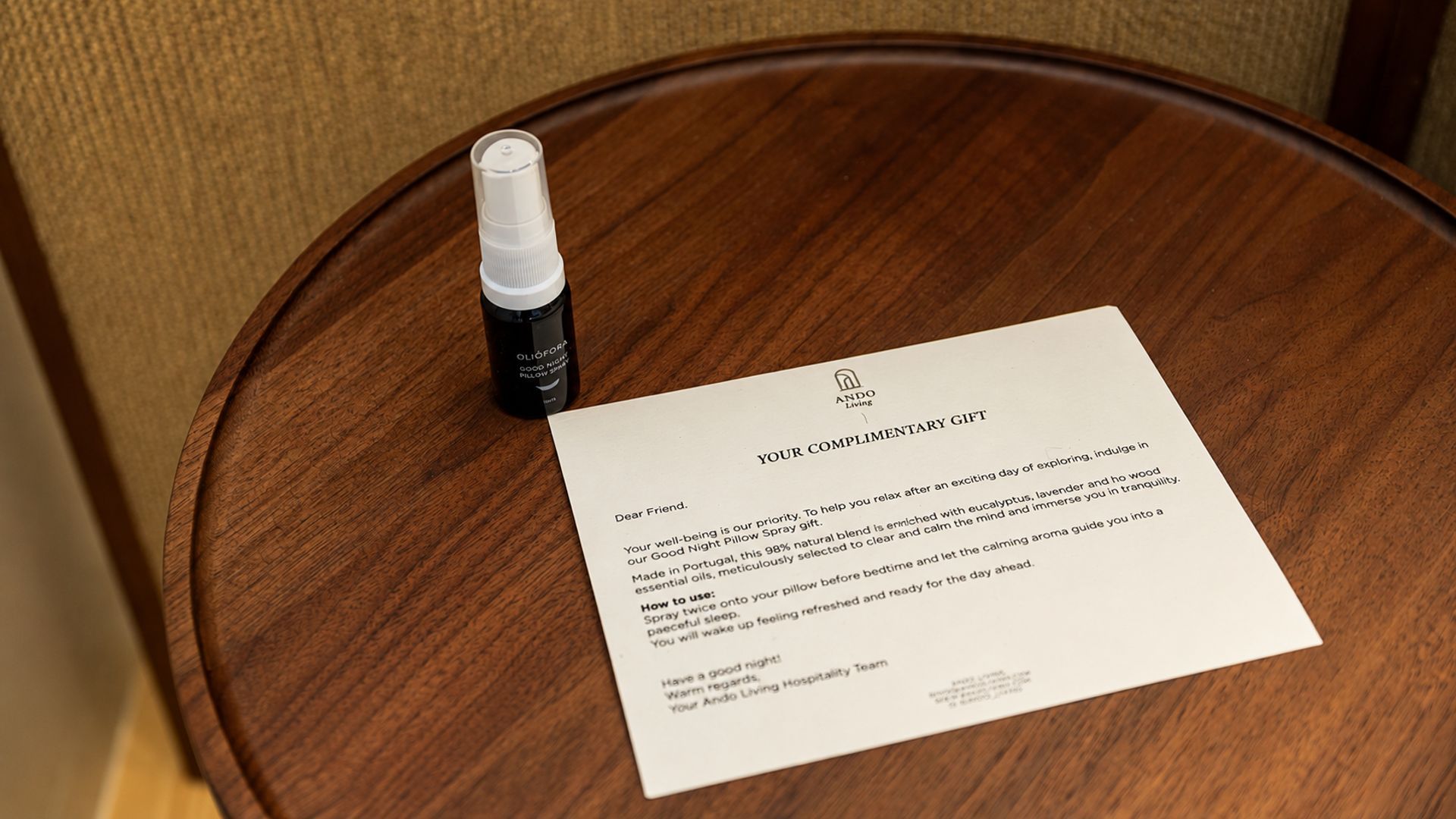 A wooden table with a pillow spray bottle and a thank you note.