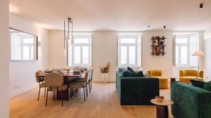 A spacious living area with a dining table set for four, a green sofa, a yellow armchair, and a small round table with a bowl. - Ando Living - Tejo Palace - 301 (Lisboa)