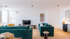 Ein modernes Wohnzimmer mit zwei grünen Sofas, einem Flachbildfernseher, einem kleinen Tisch und einer Lampe.