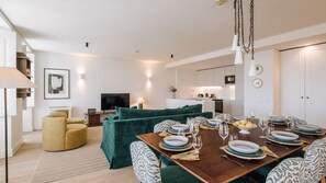 Un saló modern amb un sofà, una taula de dinar preparada per a sis i una cuina al fons.