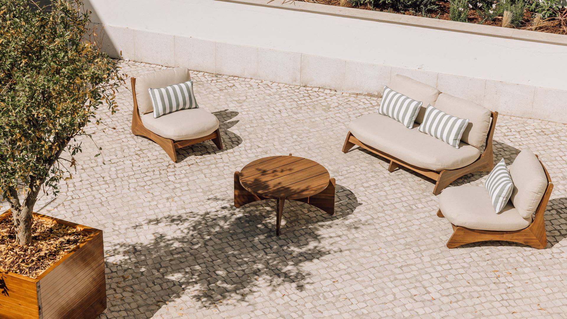 Un espace extérieur aménagé avec une table en bois, deux canapés et des chaises, entouré d’un sol pavé et d’un petit mur blanc.