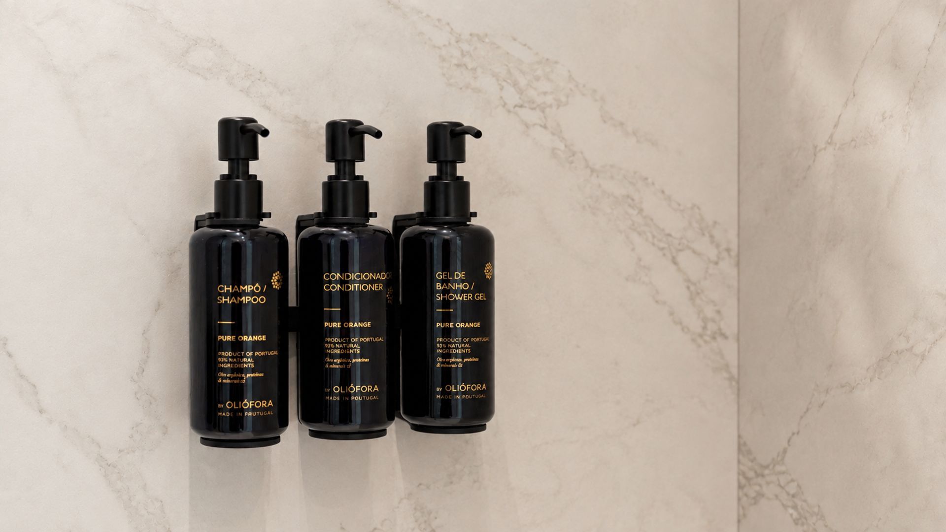 Tres botellas negras de productos OLIÓFORA frente a una pared de mármol.