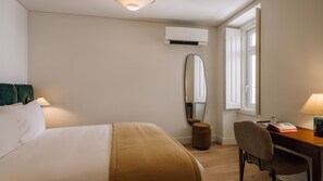 Habitació d'hotel amb un llit, escriptori, cadira, mirall, aire condicionat i finestra.