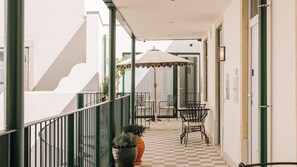 A corridor with a checkered floor, a covered outdoor seating area with chairs and a table, and a potted plant. - Ando Living - Tejo Palace - 302 (Lisboa)