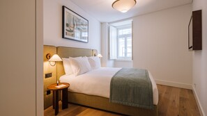 A hotel room with a bed, bedside lamps, a small table, a window, and a wall-mounted artwork. - Ando Living - Tejo Palace - 304 (Lisboa)