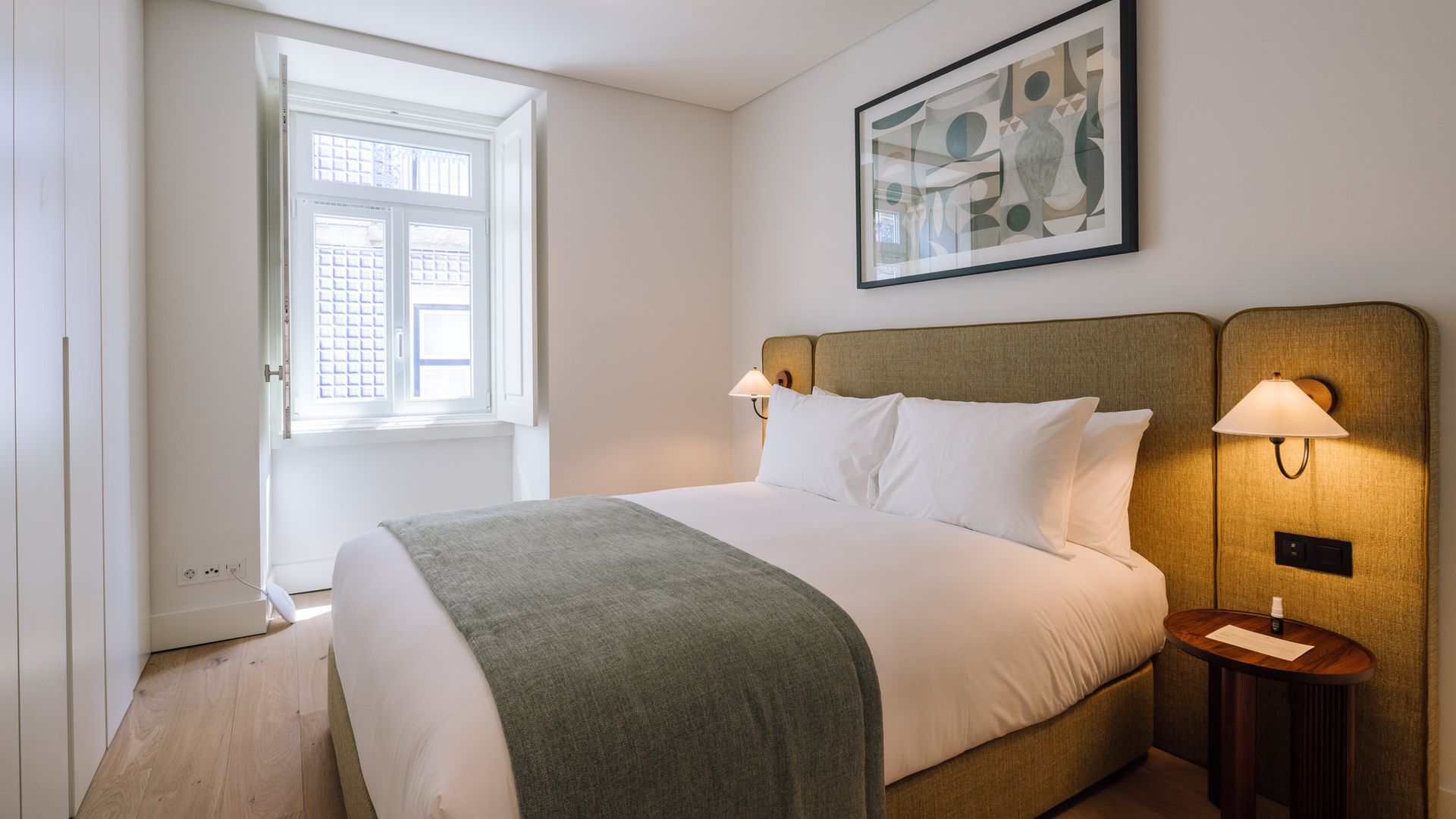 Una camera d'albergo con un letto, lampade da comodino, una finestra e un quadro astratto appeso al muro.