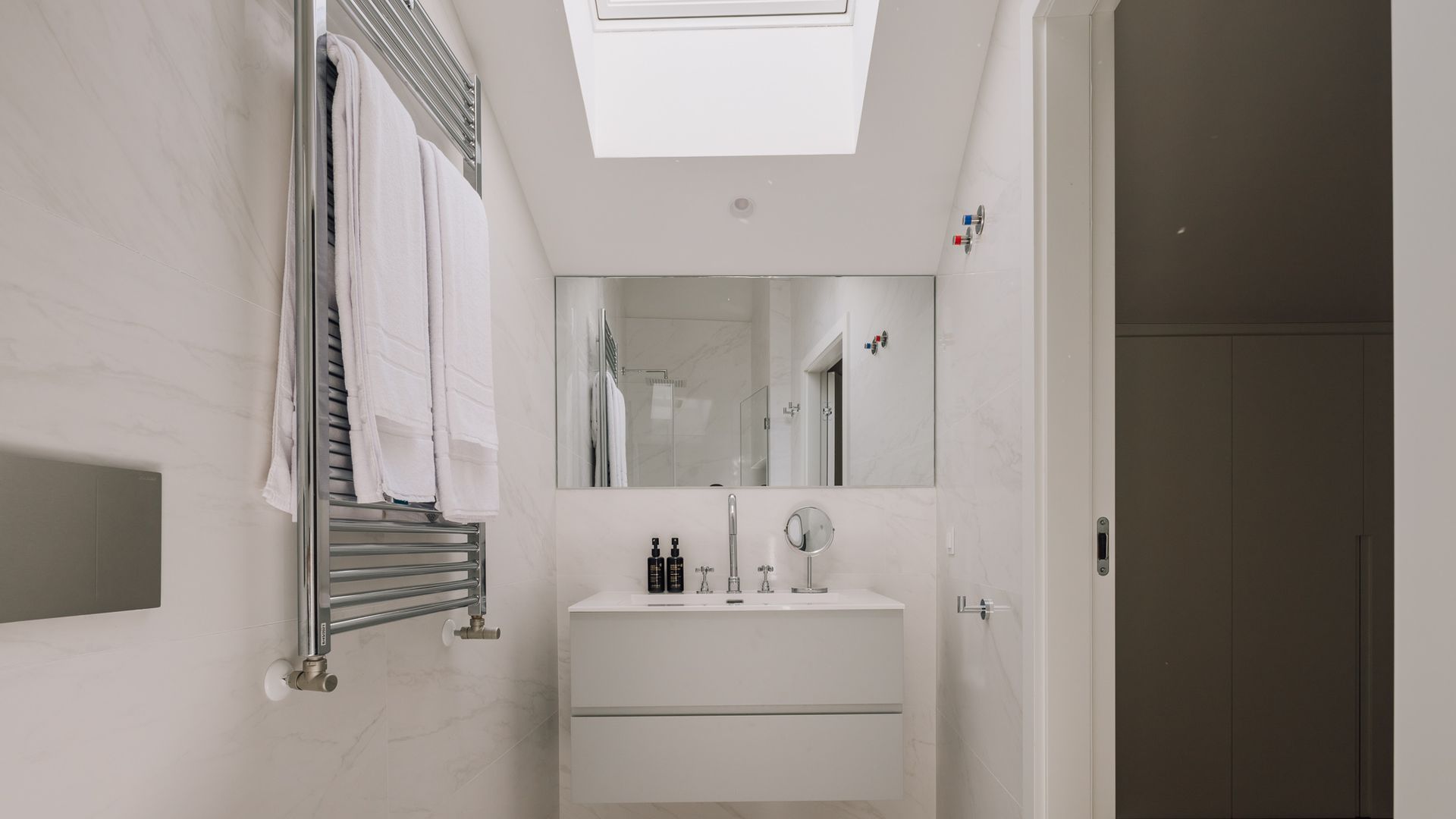 A modern bathroom with a skylight, a towel rack, a sink with toiletries, and a mirror.