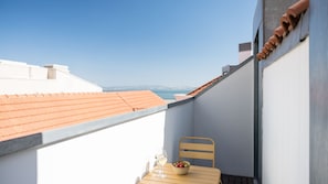 A balcony with a table, two chairs, a bowl of fruit, and a glass of wine. - Ando Living - Tejo Palace - 400 (Lisboa)