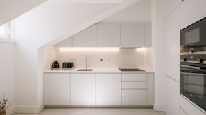 A modern kitchen with white cabinetry, a built-in oven, and a coffee maker. - Ando Living - Tejo Palace - 400 (Lisboa)