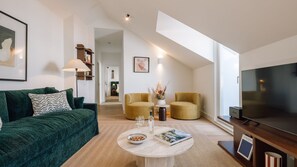 A modern living room with a green sofa, two armchairs, a coffee table with a book and glasses, and a TV on a wooden stand. - Ando Living - Tejo Palace - 400 (Lisboa)
