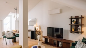 A modern living room with a flat-screen TV, a wooden coffee table, and a dining area with a table set for two. - Ando Living - Tejo Palace - 401 (Lisboa)