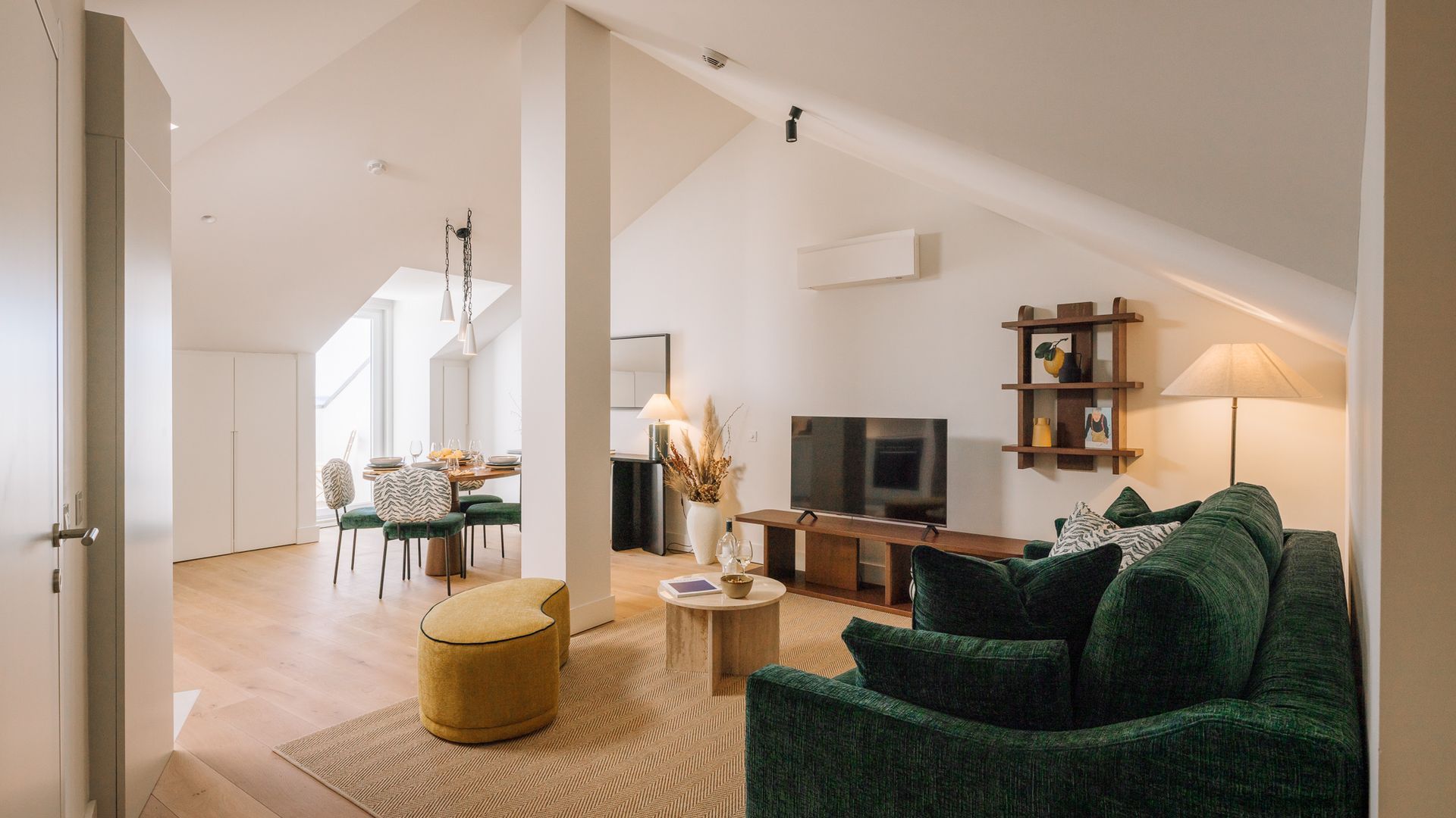 A modern living room with a green sofa, a television, and a dining area with a table and chairs.