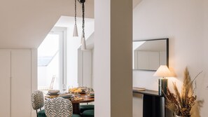 A modern interior with a dining area featuring a table set for two, a green upholstered chair, and a hanging light fixture. - Ando Living - Tejo Palace - 401 (Lisboa)