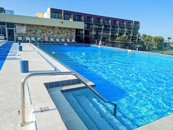 Una piscina amb una paret de pedra i un edifici de diversos pisos al fons.