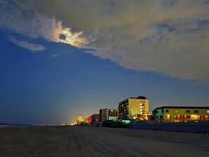 Hotel a primera línia de platja amb diversos edificis, una platja de sorra i un cel clar amb núvols.