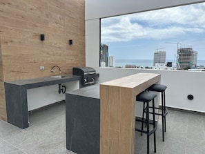 A modern outdoor kitchen with a built-in grill and bar area, overlooking a cityscape with buildings and the sea. - Modern STUDIO in a central, tourist-friendly area of the city (Manta)