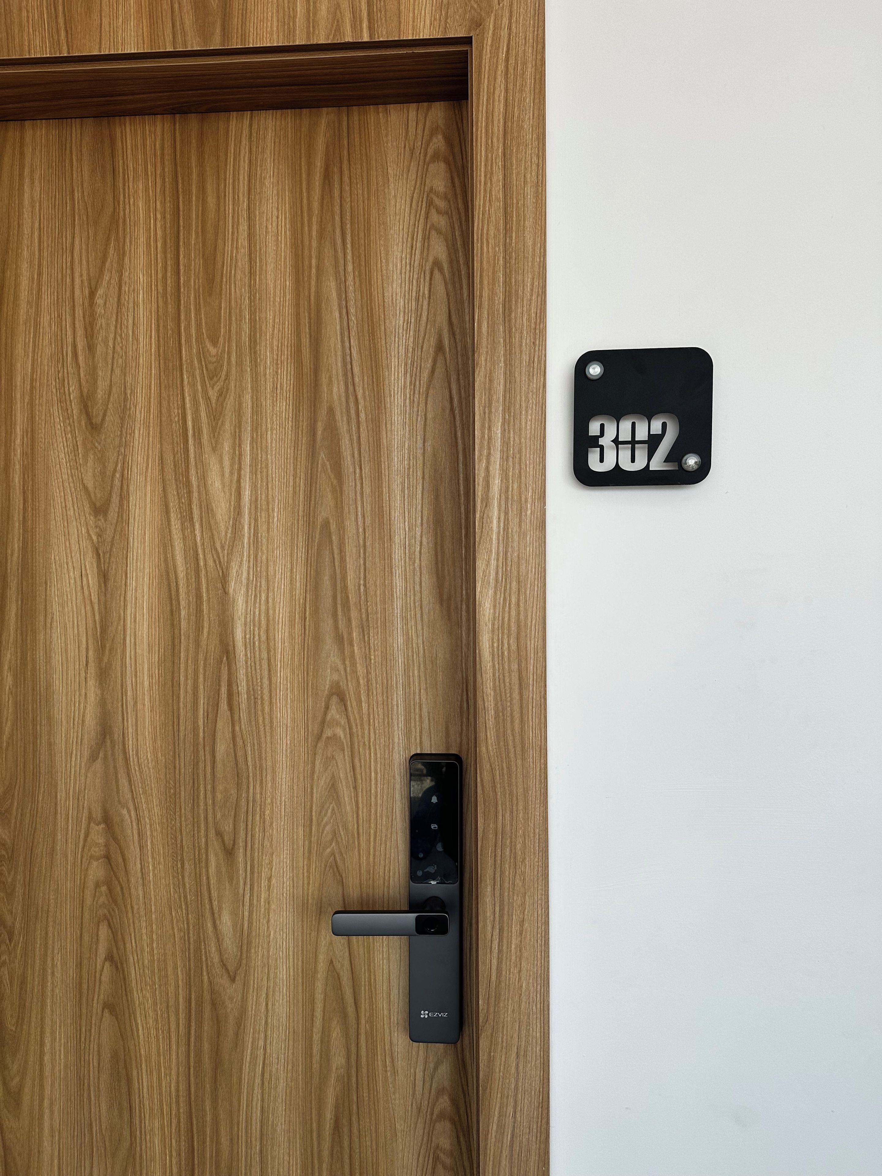 A wooden door with a black doorbell and a black plate with the number 302.