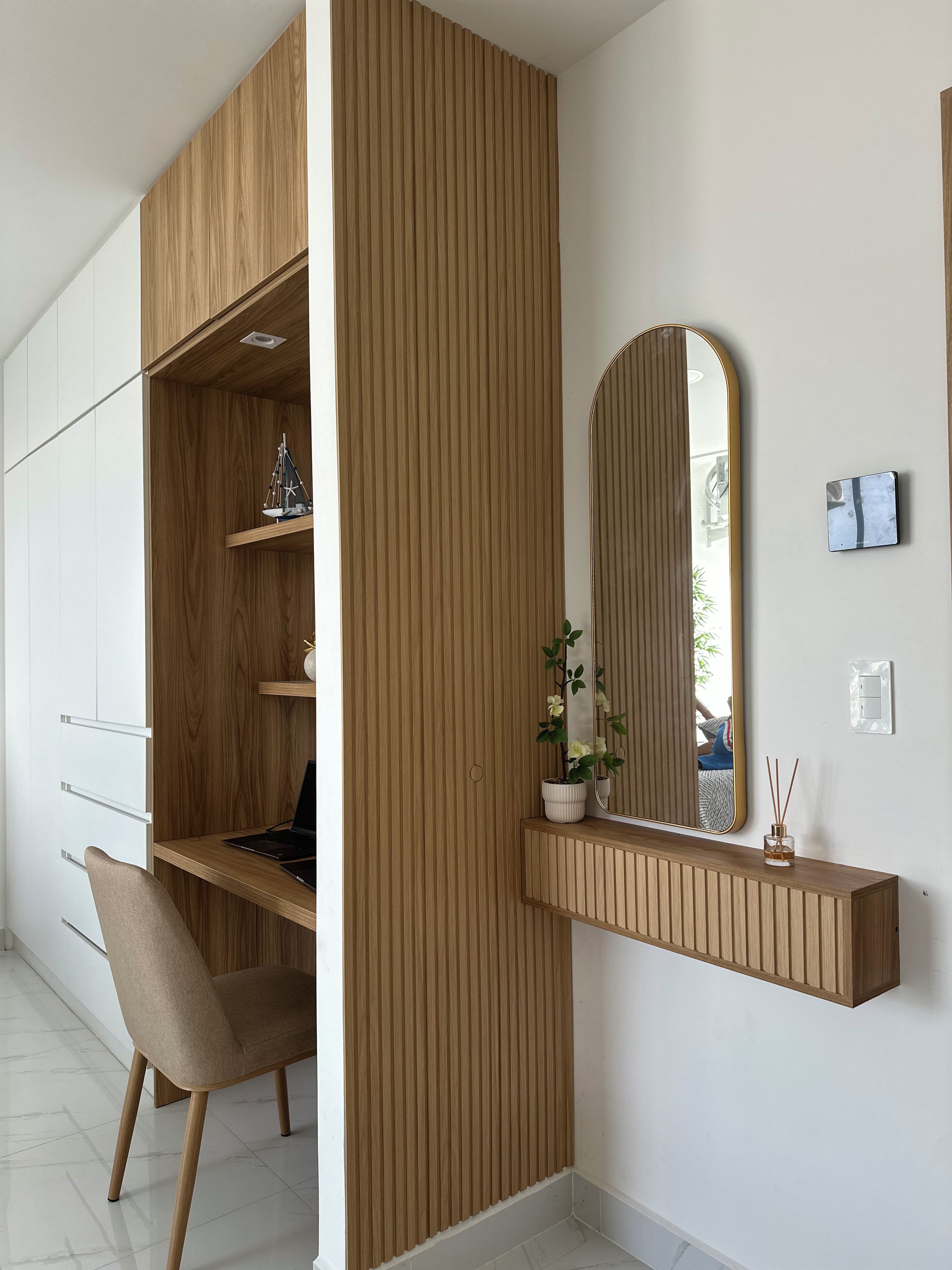 Une chambre moderne avec un bureau en bois, une chaise, un miroir et une petite étagère sur laquelle est posée une plante.