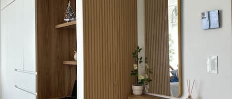 Una habitación moderna con un escritorio de madera, una silla, un espejo y una pequeña estantería con una planta.