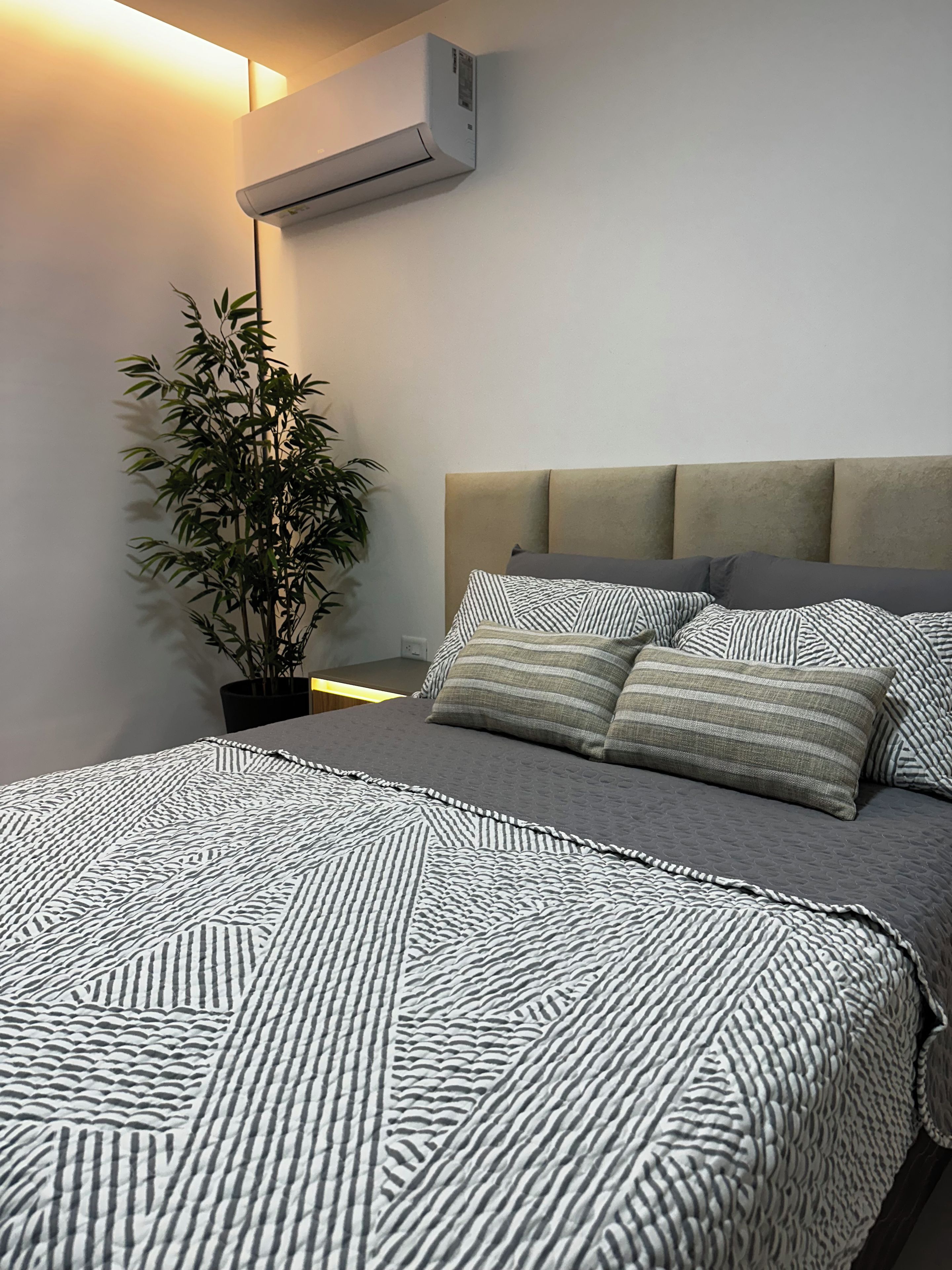 Ein modernes Schlafzimmer mit Bett, Kopfteil, einer Topfpflanze und einer Klimaanlage.