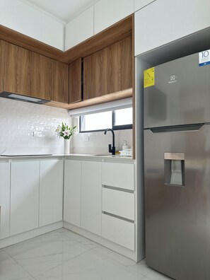 A kitchen with white cabinets, a stainless steel refrigerator, a black faucet, and a window above the sink. - Modern STUDIO in a central, tourist-friendly area of the city (Manta)