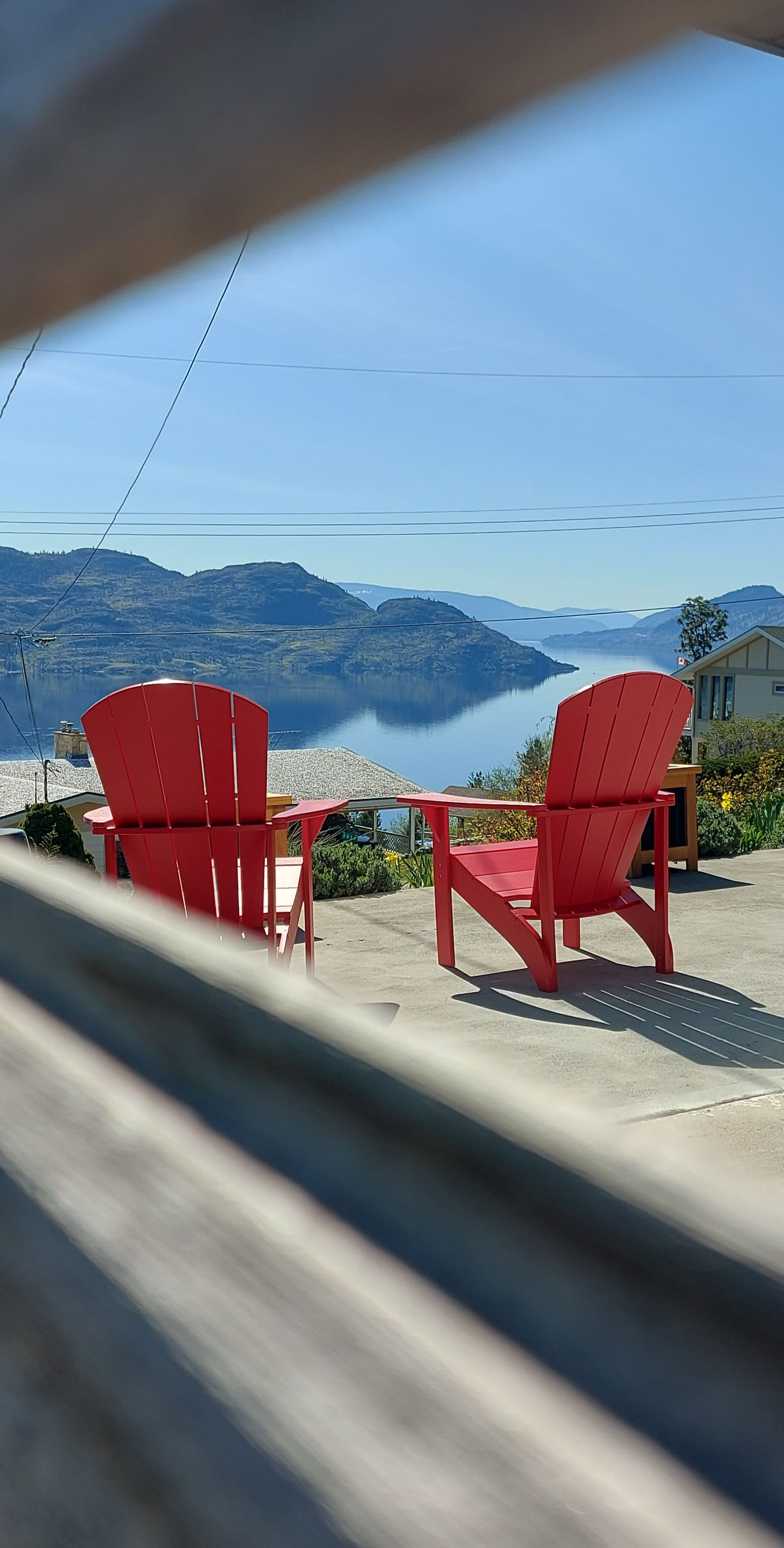 Two red Adirondack chairs facing a lake with mountains in the background.