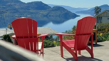 Two red Adirondack chairs facing a lake with mountains in the background.