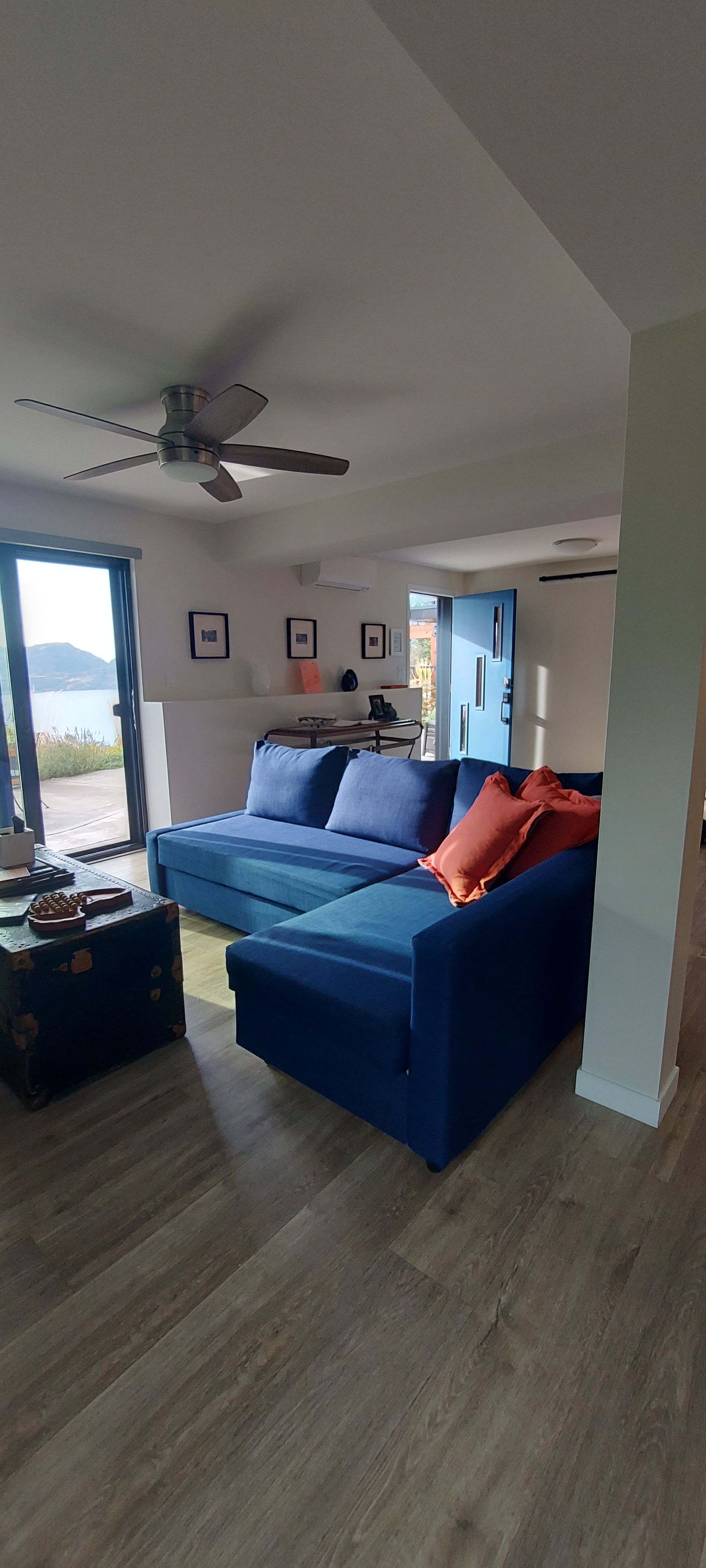 Una sala de estar moderna con un sofá modular azul, un ventilador de techo y un amplio ventanal con vistas.