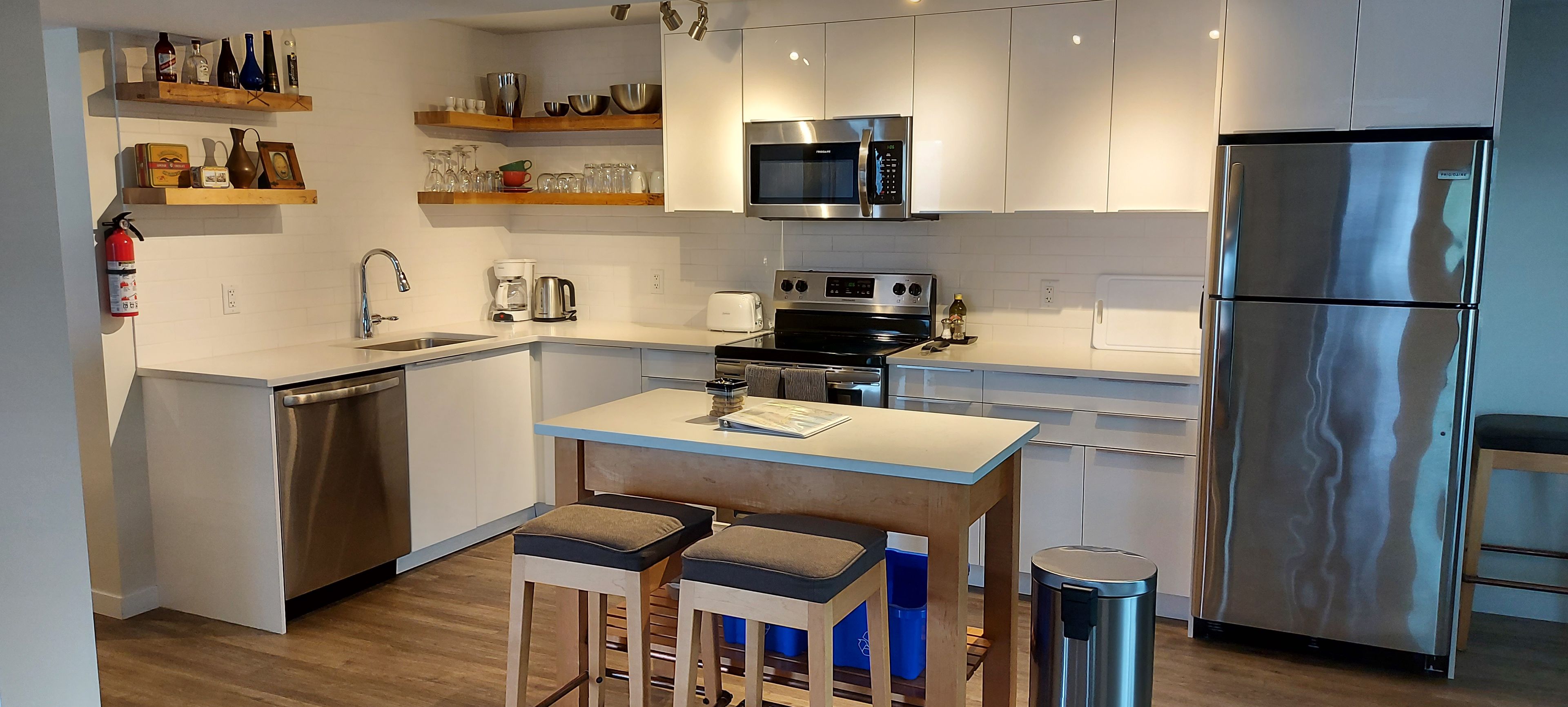 Une cuisine moderne dotée d’appareils électroménagers en acier inoxydable, de tabourets de bar en bois et d’étagères intégrées.