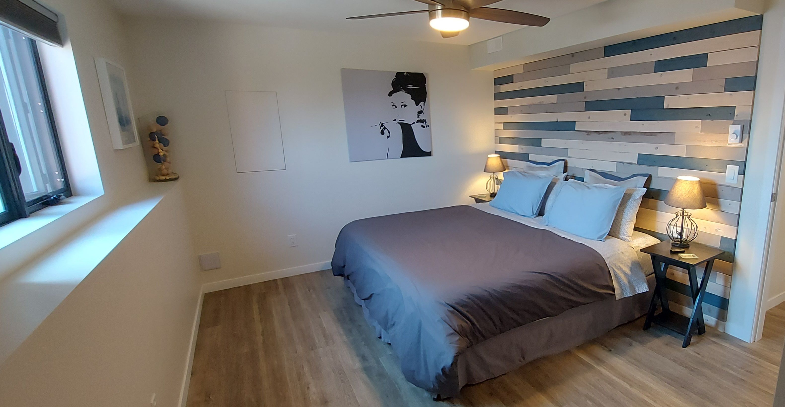A bedroom with a bed, bedside tables, a ceiling fan, a window, and a wall with a geometric pattern.