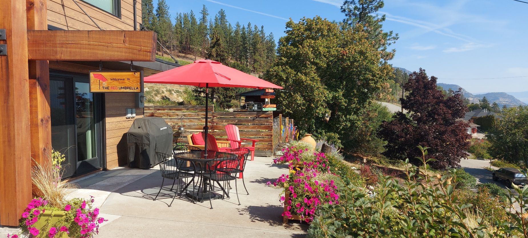 A wooden building with a red umbrella, outdoor seating, and a sign welcoming to The Red Umbrella.