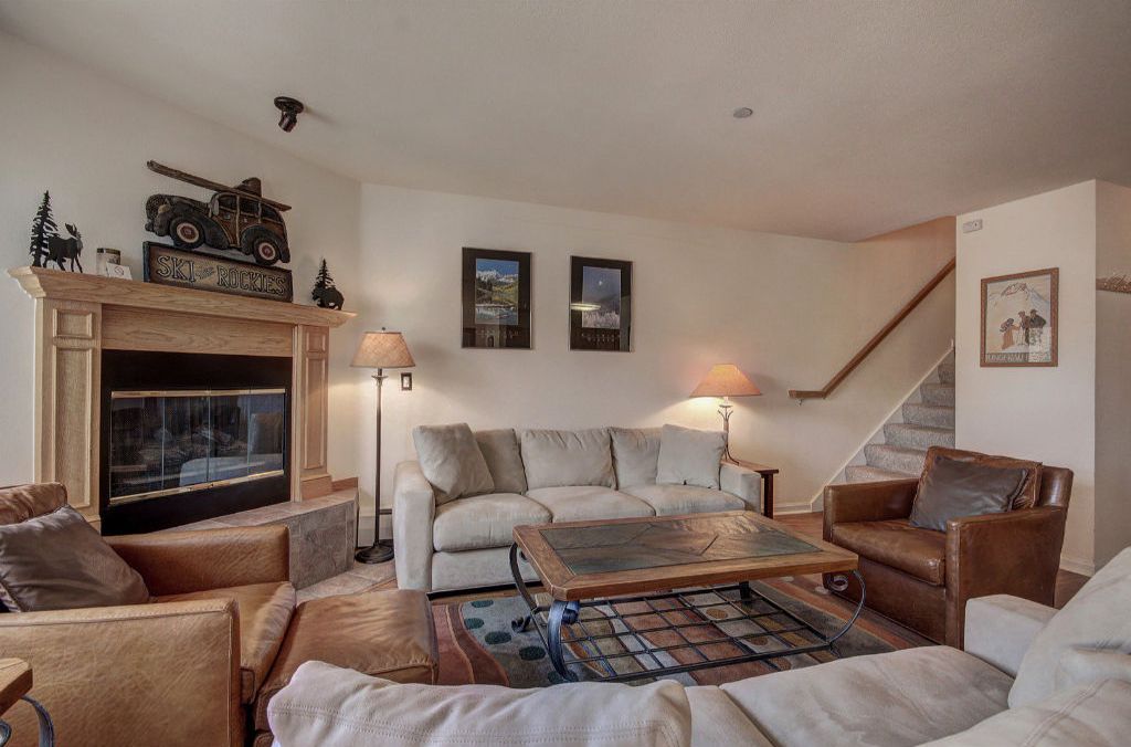 Un salon chaleureux avec une cheminée, un ensemble de canapés, une table basse et deux lampes fixées au mur.