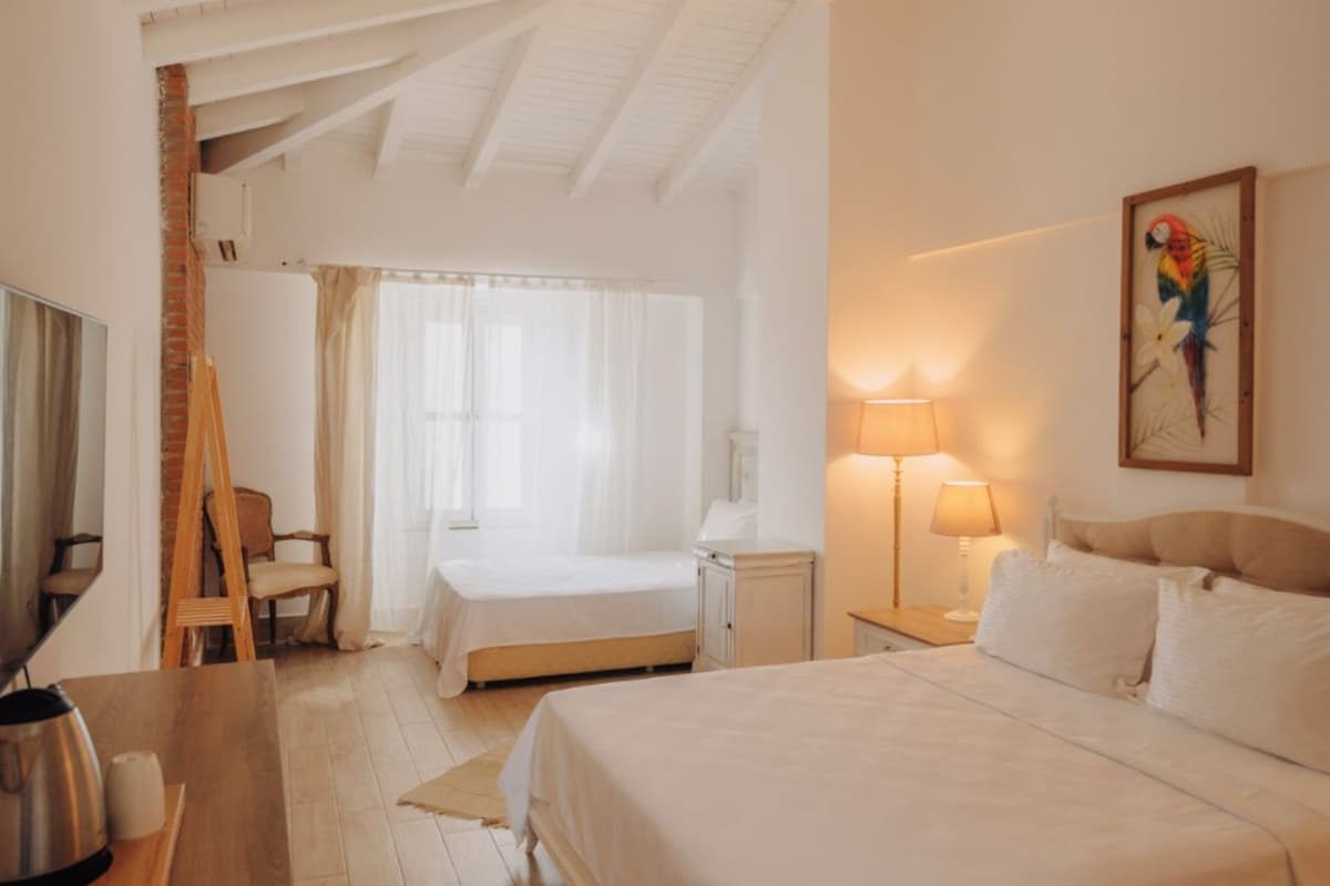 Un dormitorio amplio con una cama grande, un escritorio de madera, una silla, una lámpara y un cuadro en la pared.