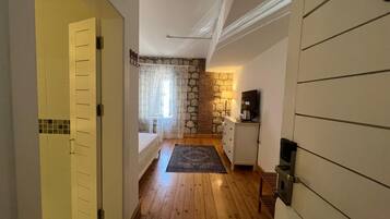 Un pasillo estrecho que conduce a un dormitorio con pared de piedra, una cama, un aparador y un televisor.