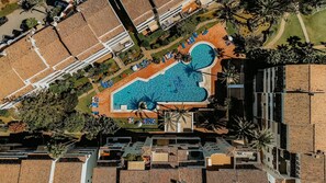 An aerial view of a resort with a central swimming pool surrounded by lounge areas and palm trees. - 03 Beach Home by Abarzo (Marbella)