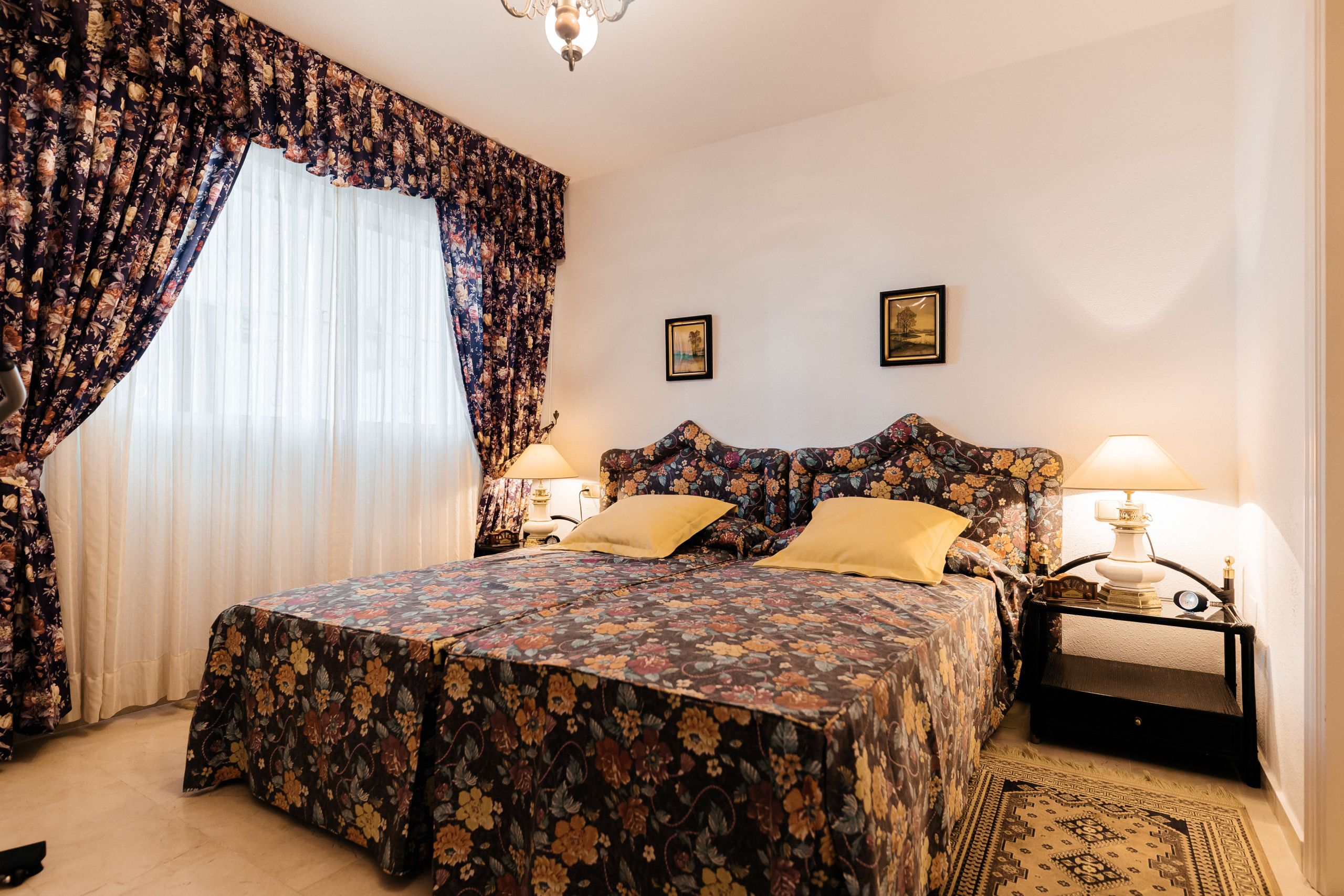 A bedroom with a large bed, floral curtains, two bedside lamps, and a rug.