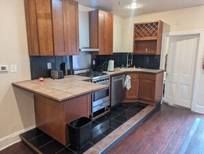 A kitchen with wooden cabinets, a stove, a sink, and a trash bin. - Cozy 1-bedroom apartment in charming Philadelphia with AC (Philadelphia)