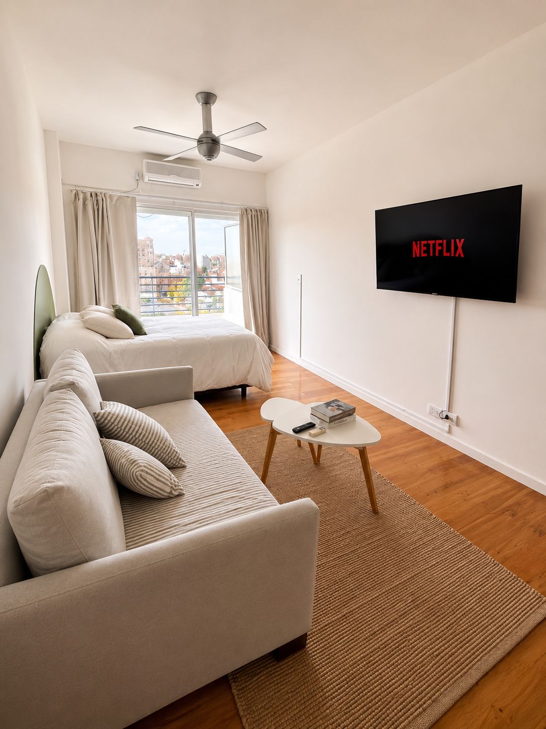 A modern bedroom with a bed, a sofa, a TV, and a ceiling fan.